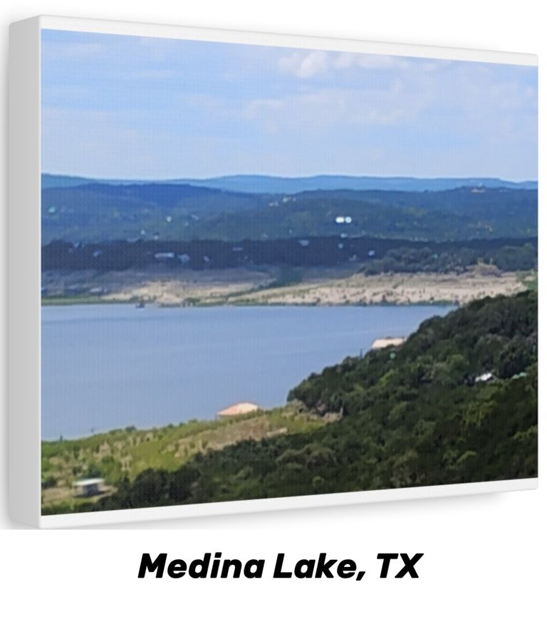 A framed canvas print, shown at a slight angle, of a view across Medina Lake in the Texas Hill Country: still blue water below a limestone shoreline, wooded hills receding into haze, and a scattering of hilltop homes under a partly cloudy sky. A caption beneath the canvas reads “Medina Lake, TX”.